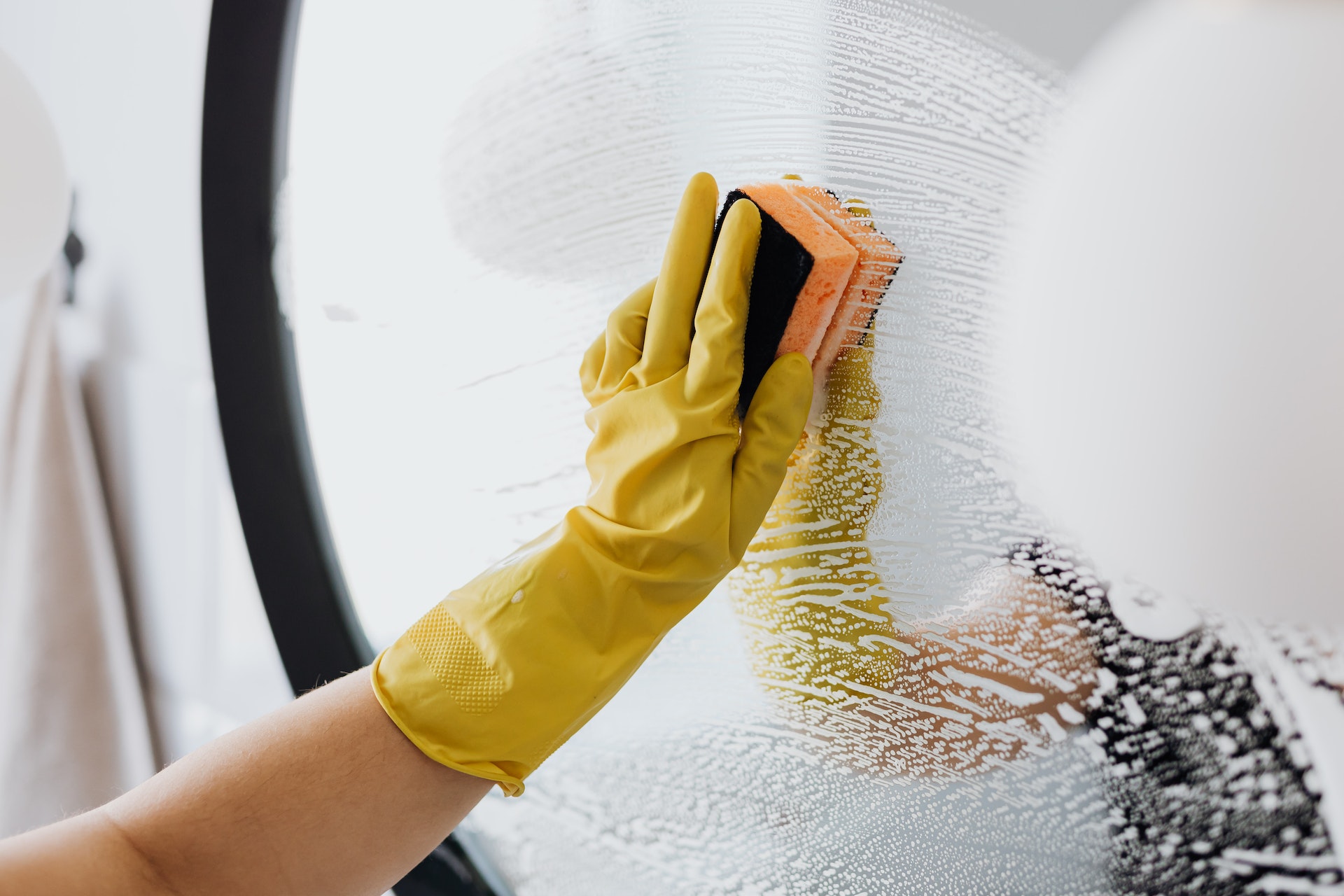 A woman wearing yellow cleaning gloves wiping a mirror