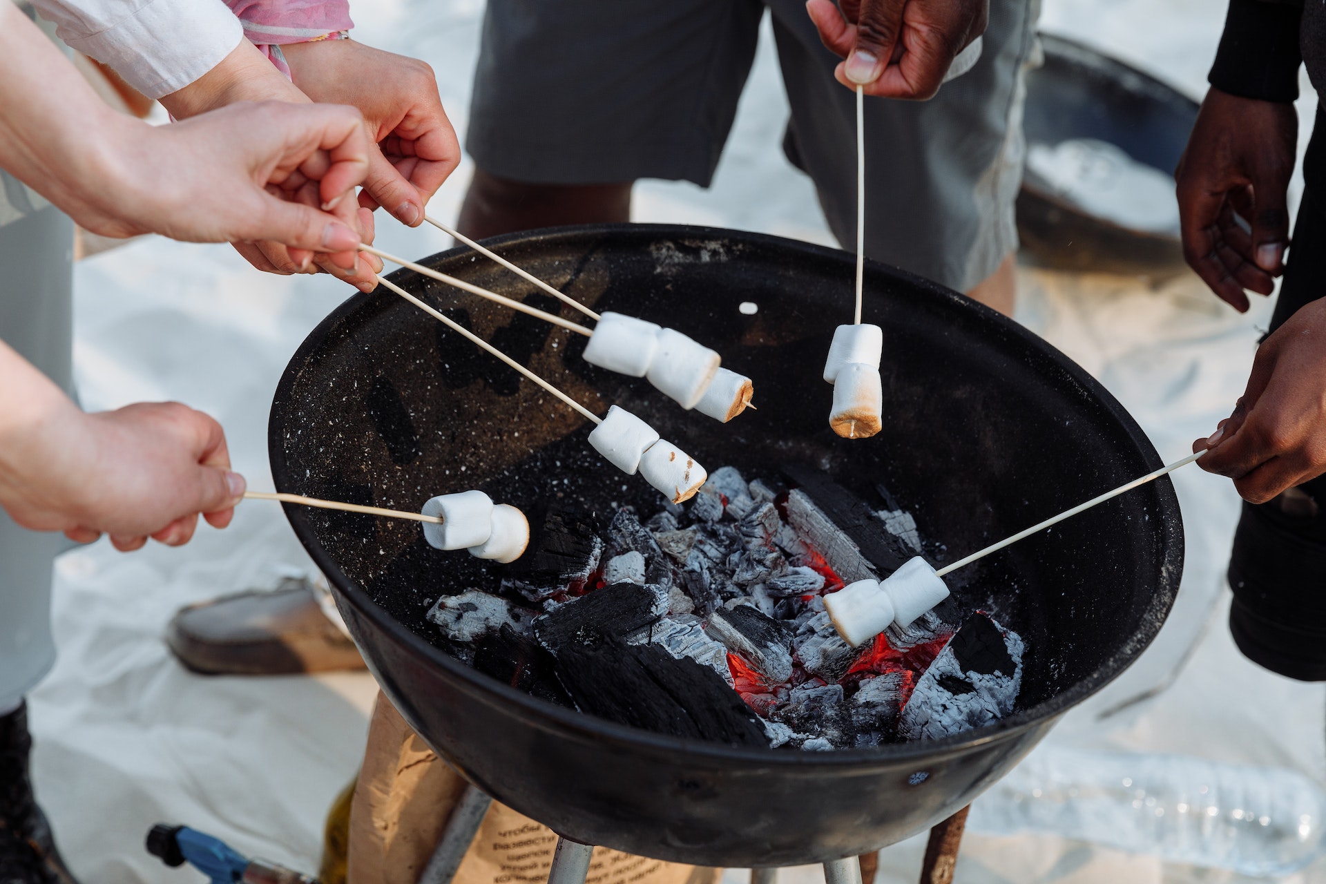 A photo of friends holding skewers of marshmallows over a beach fire pit