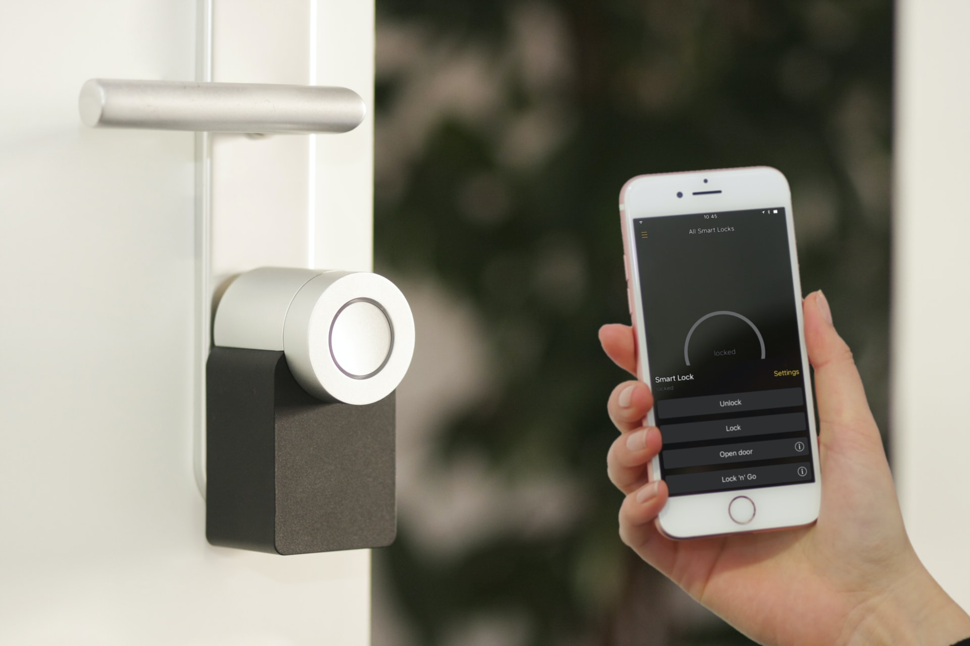 Someone holding a smartphone next to a smart lock on a silver door.