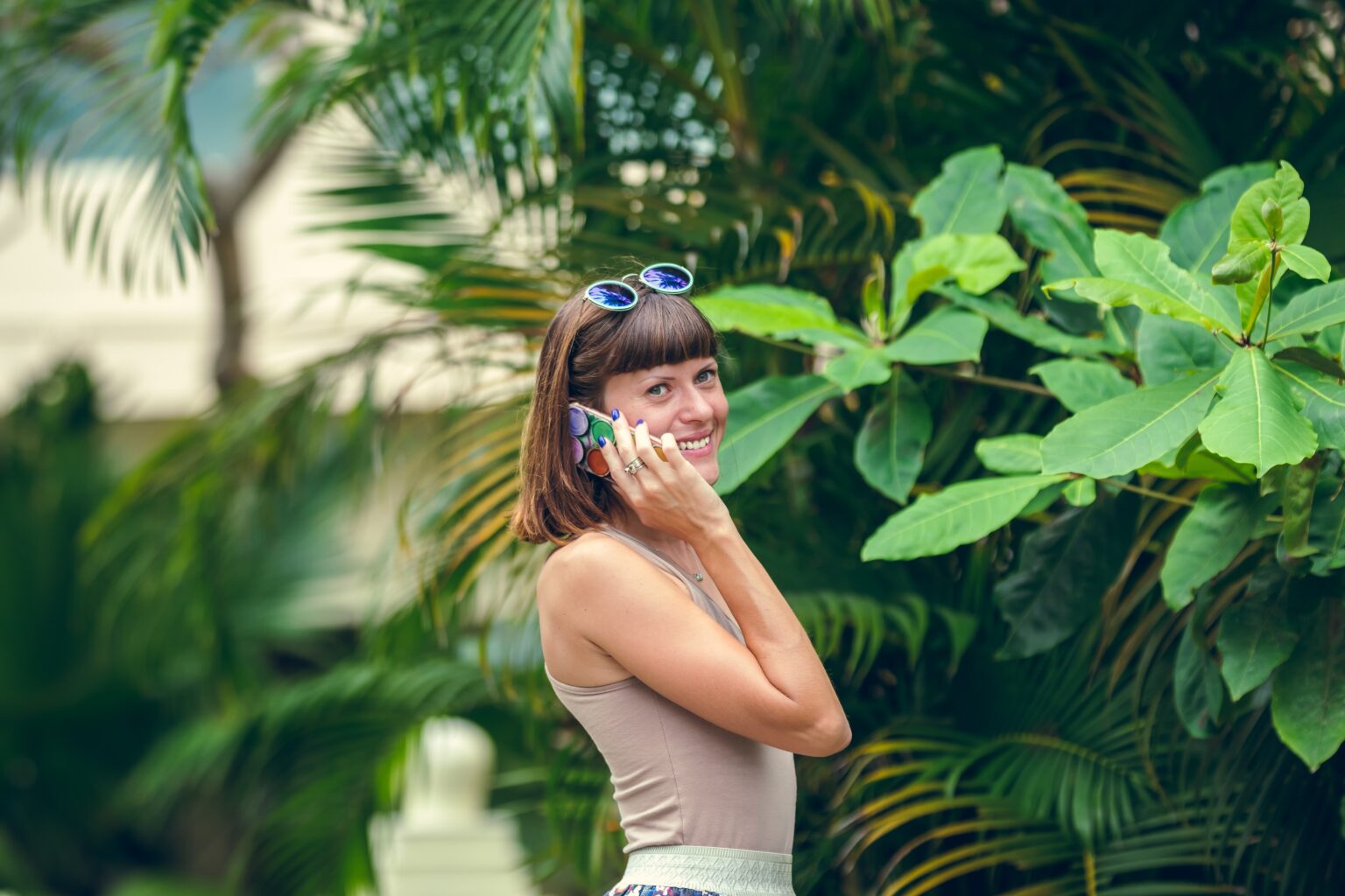 Woman talking on phone in the middle of tropical plants with a hat on