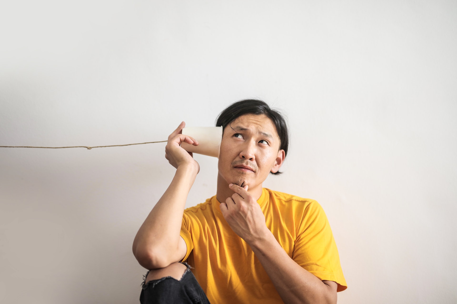 A man holds a cup to his ear attached to a string, to suggest poor communication.