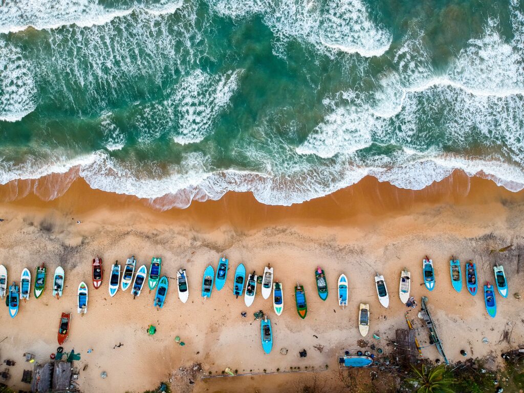 boats docked on the beach with the waves from a sky view