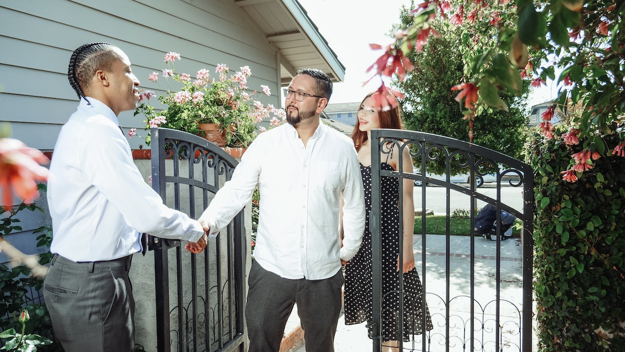 Three people at the entrance of a property, two of whom are shaking hands.