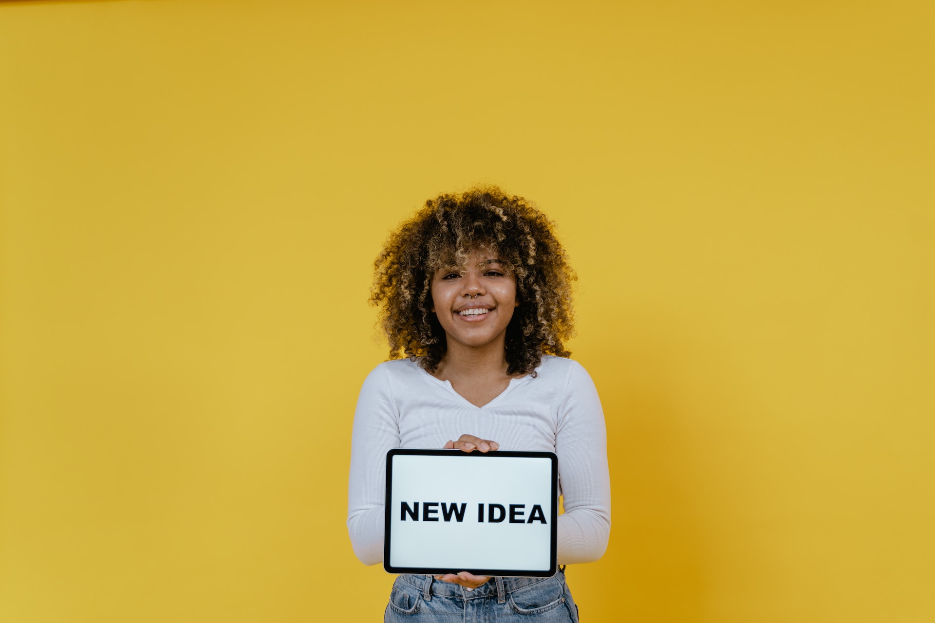  A photo of a woman holding a tablet saying ‘new idea’ against a yellow background